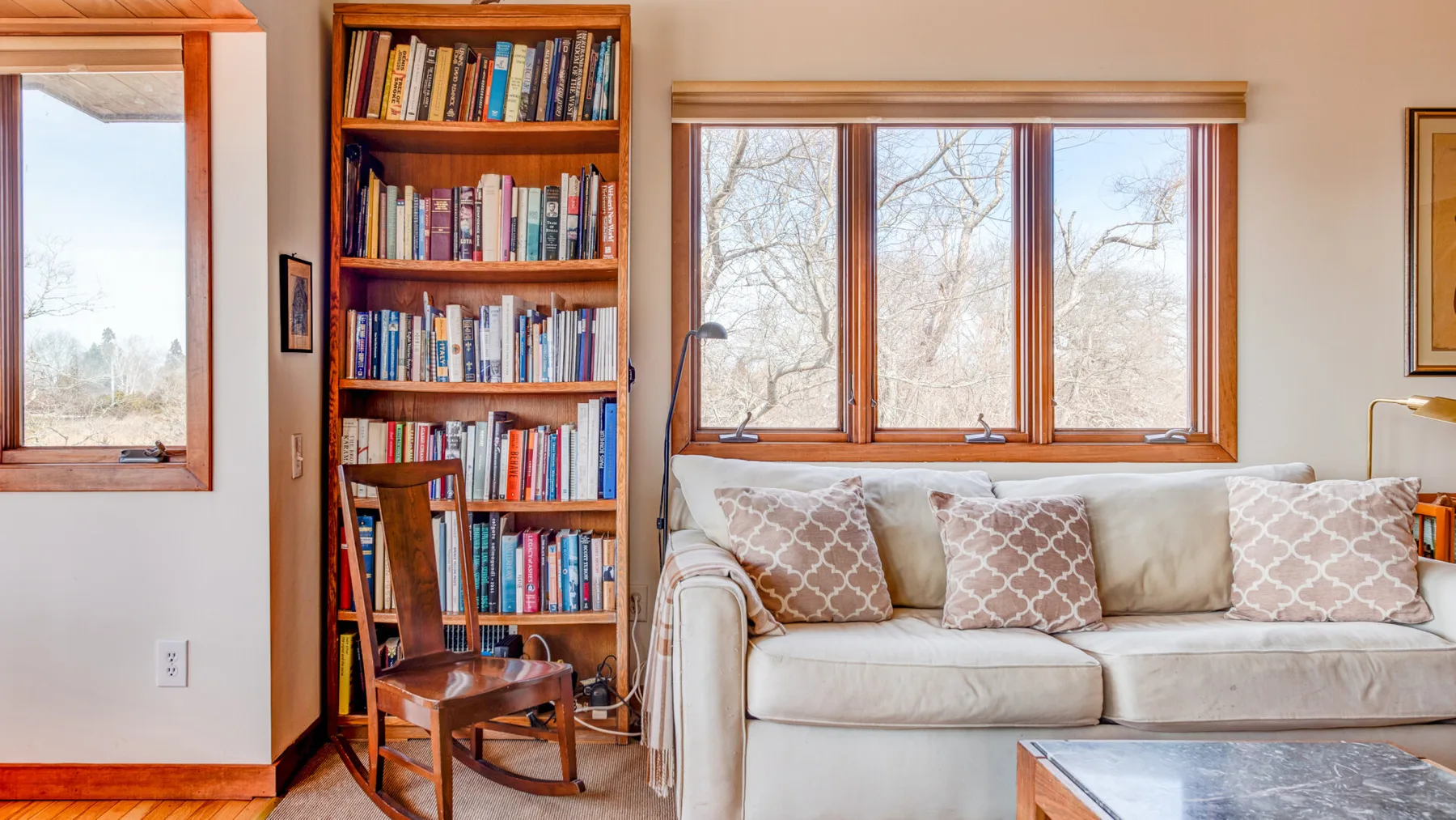 A bright living room with a cream sofa and a bookcase beside the windows.