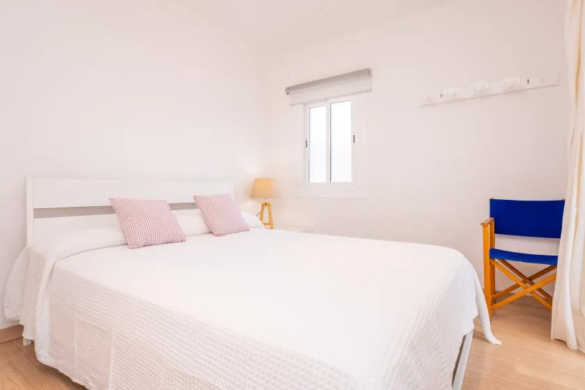 A bright bedroom with a large bed, two pillows, and a blue chair.