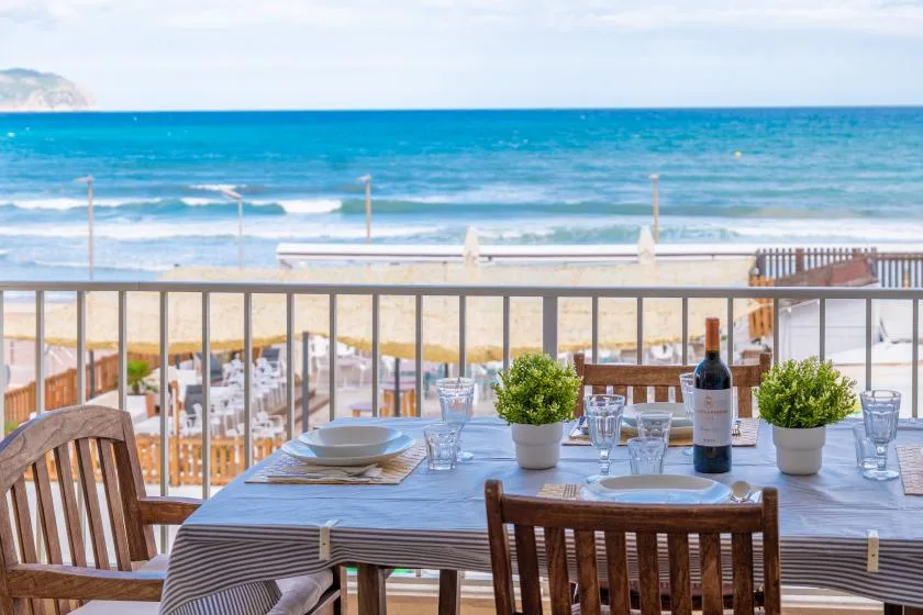 Una mesa de comedor al aire libre da a una playa de arena y al océano.