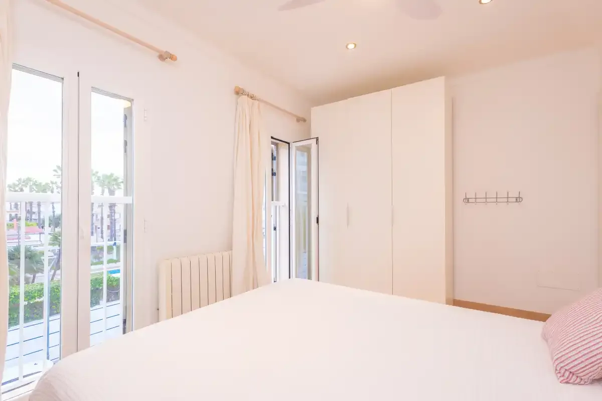 A bright bedroom with a bed, tall windows, and a wall-mounted coat rack.
