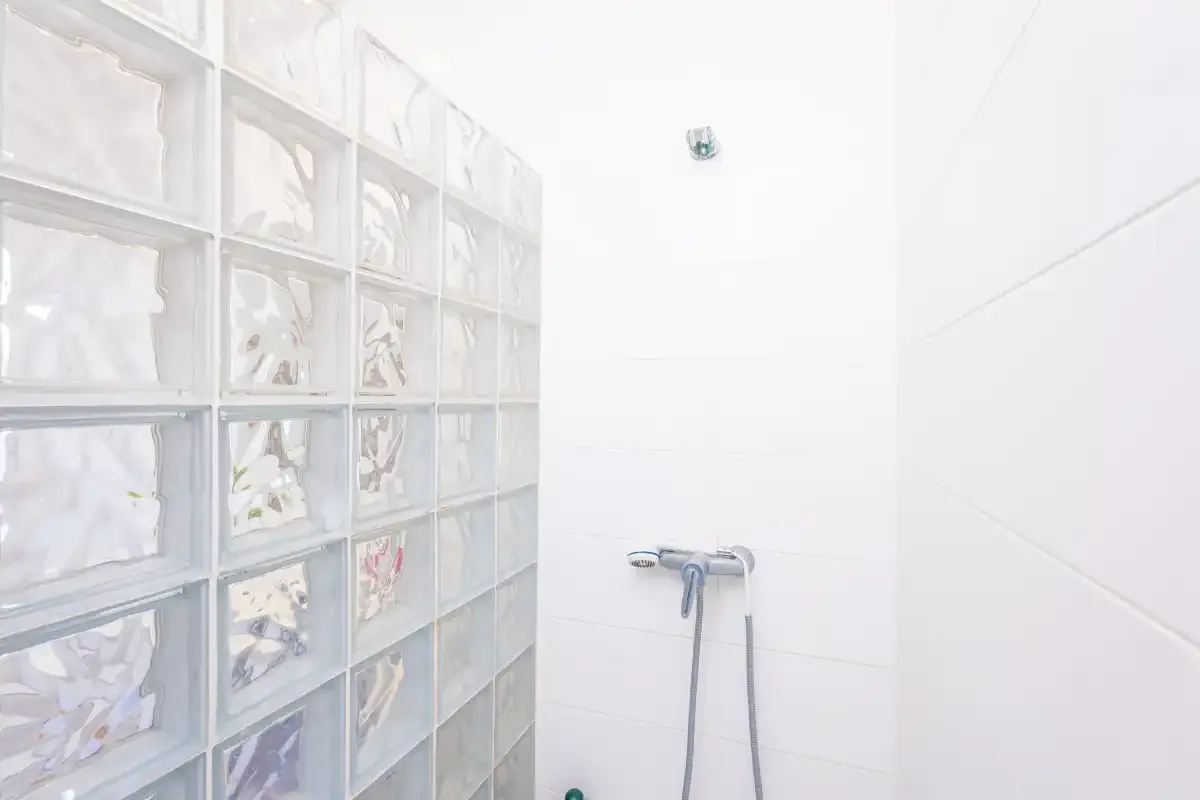 A bright tiled bathroom with a handheld shower beside a glass-block wall.