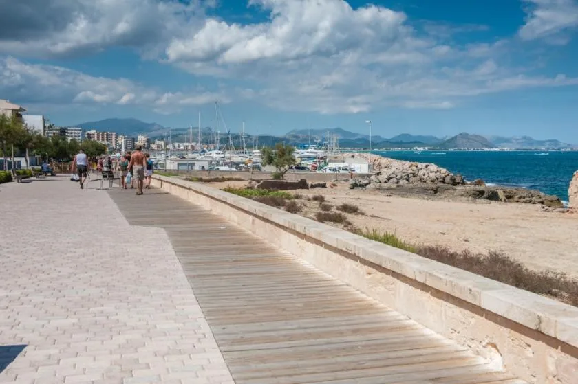 A seaside promenade with a paved walkway, wooden path, and blue water.