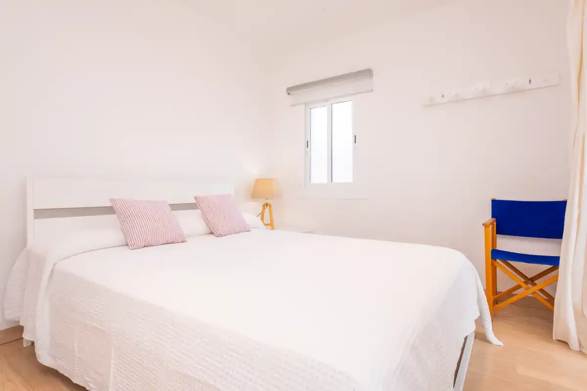A bright bedroom with a neatly made bed and a blue chair beside the window.