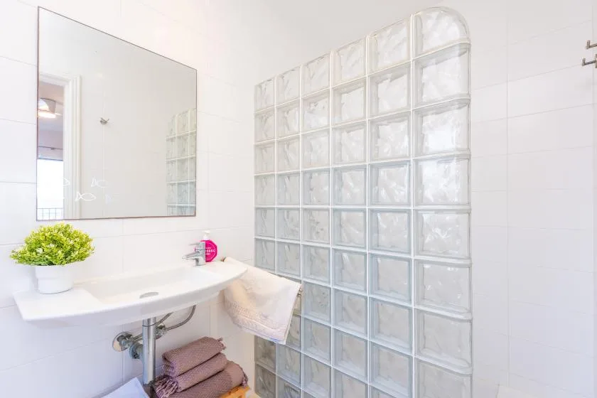 A bright bathroom with a sink, mirror, and glass-block shower wall.