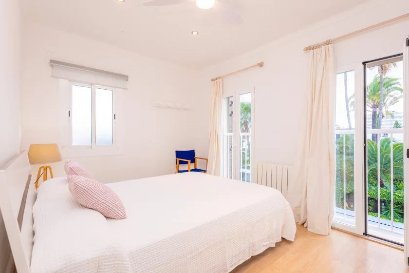 A bright bedroom with a bed and tall windows overlooking greenery.