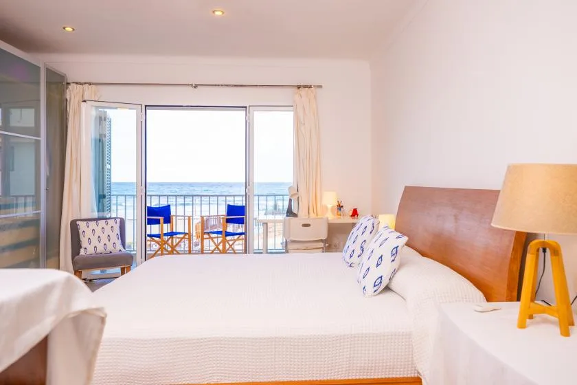 A bright bedroom with a large bed facing glass doors and a balcony overlooking the sea.