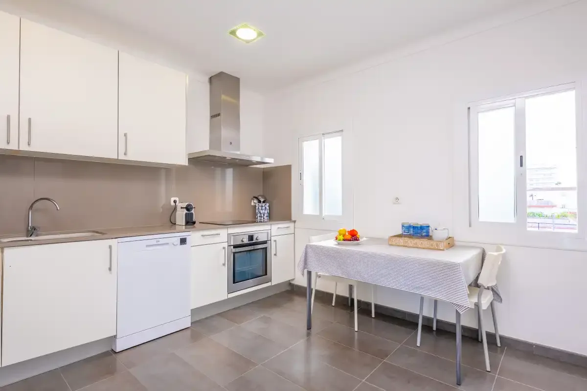 A bright kitchen with white cabinets, appliances, and a dining table by the windows.
