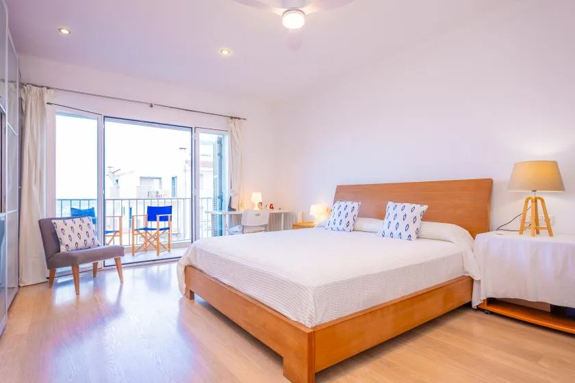 A bright bedroom with a wooden bed, bedside table, and large glass doors.