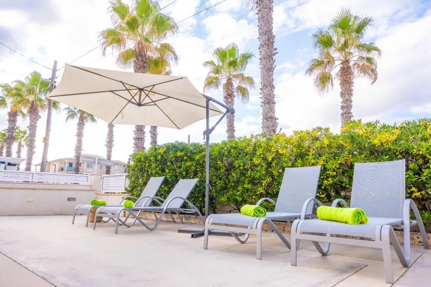 An outdoor poolside lounge area has reclining seating beneath a large umbrella.