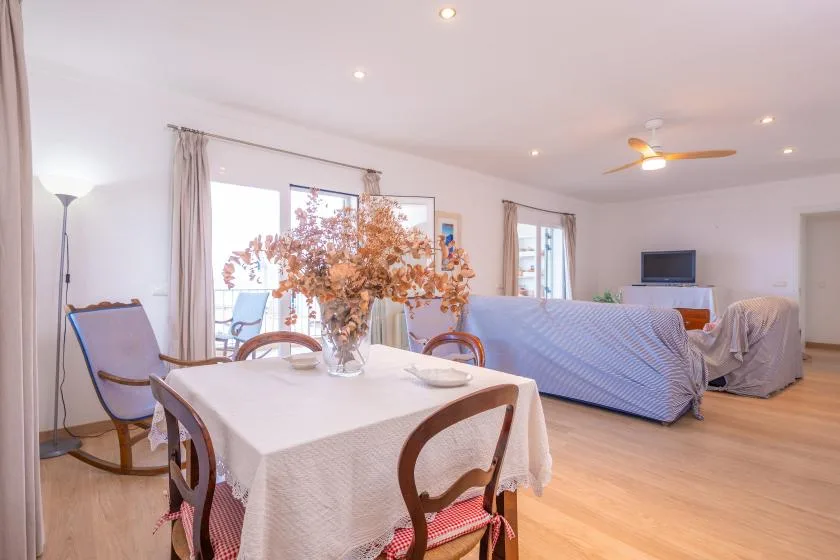 A dining table with dried flowers sits beside a living area with covered seating.