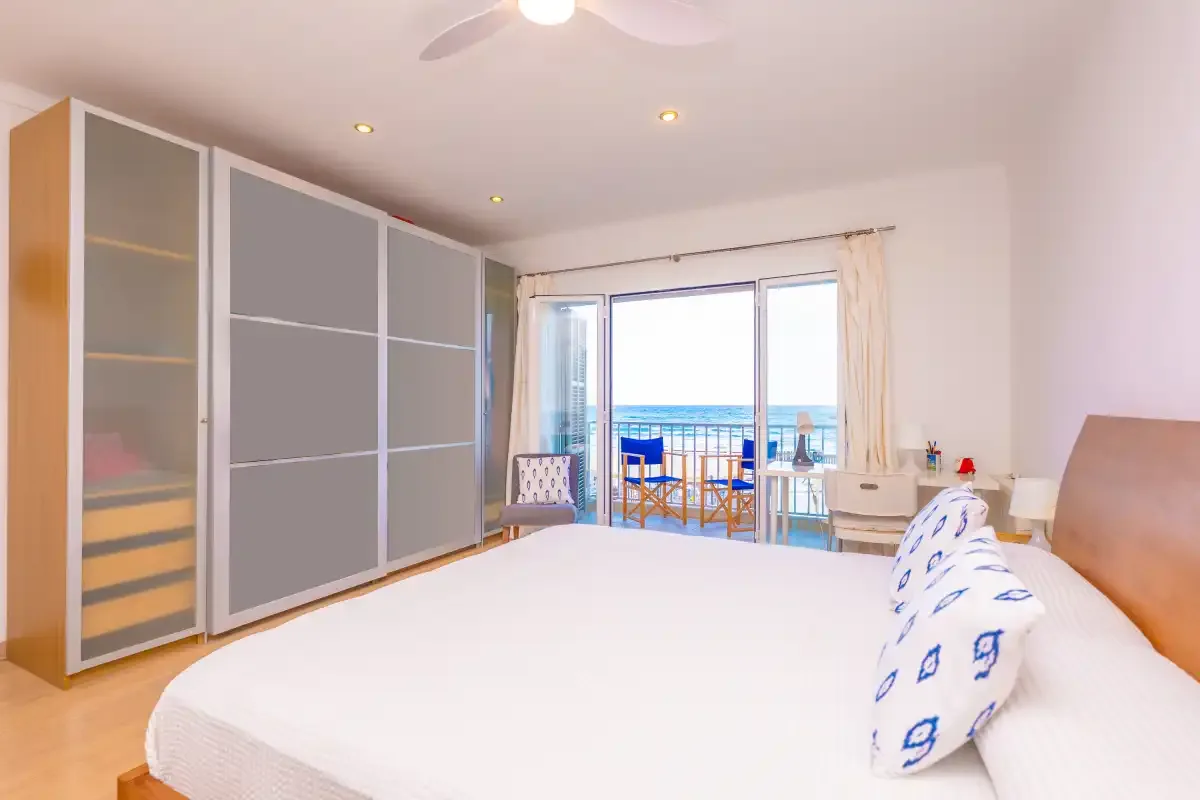 A bright bedroom with a large bed and glass doors opening to a balcony.