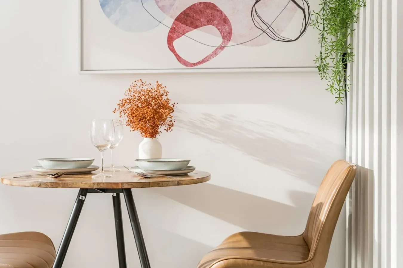 Un rincón de comedor con una mesa redonda preparada con platos junto a una silla.