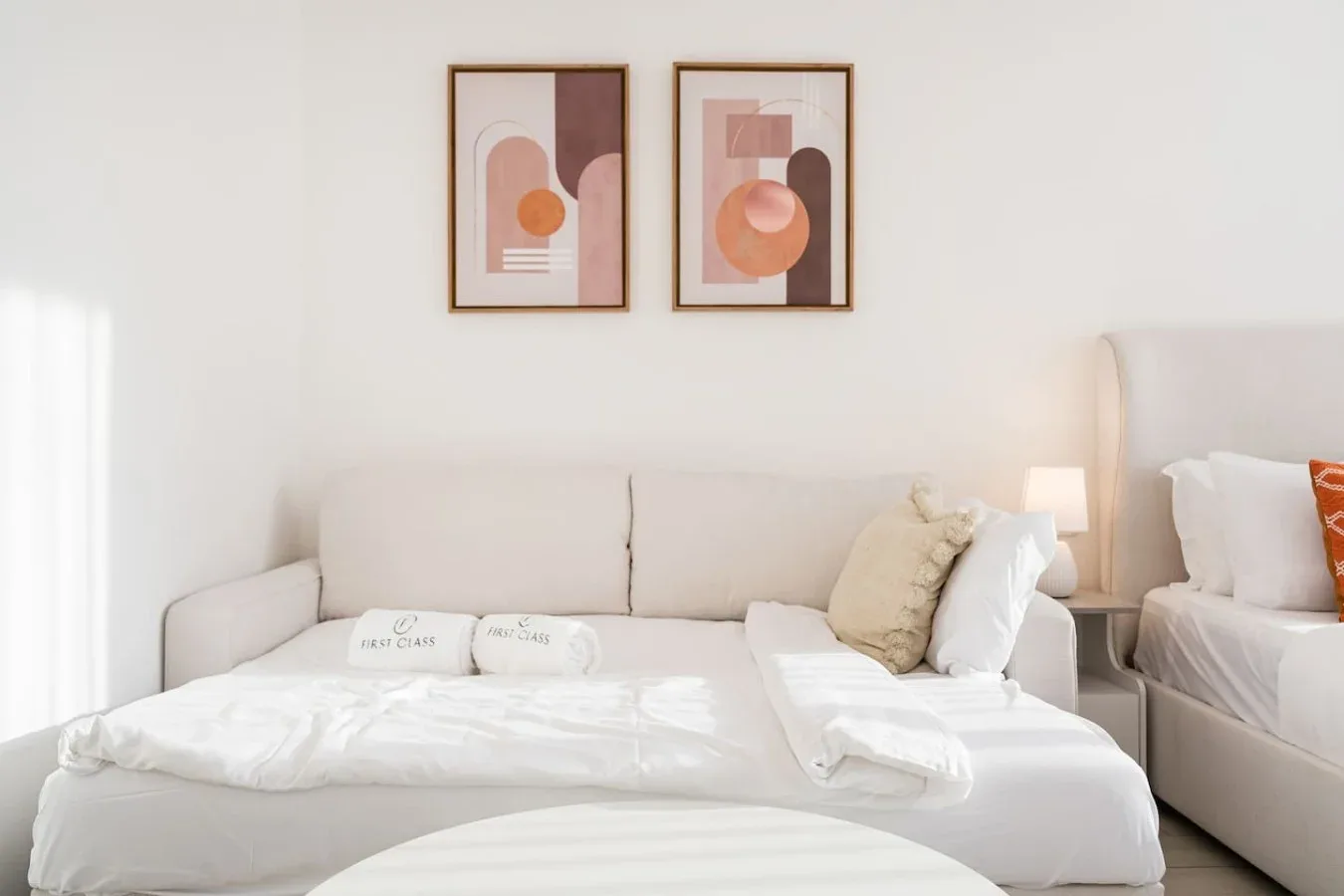 Un dormitorio luminoso con una cama bien tendida y dos cuadros enmarcados encima.