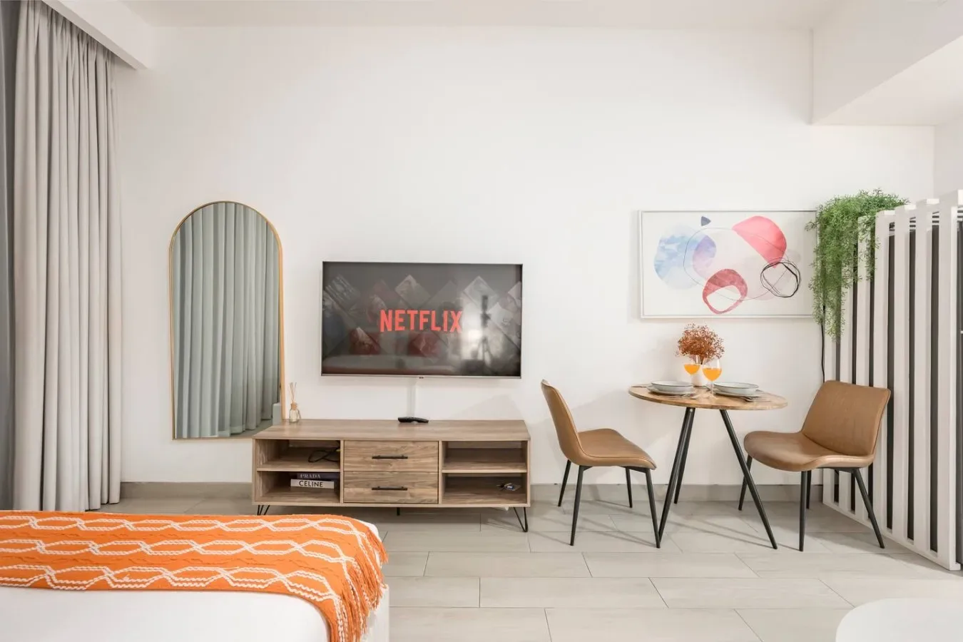 Una sala luminosa con televisor, asientos y una pequeña mesa de comedor.