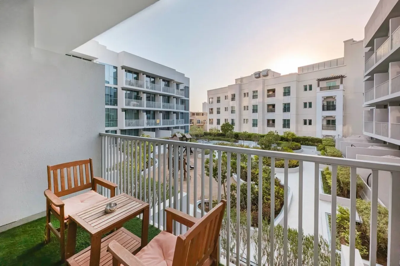 Un balcón con asientos al aire libre da a jardines y edificios de apartamentos cercanos.