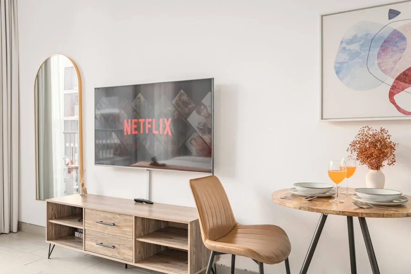 Una sala luminosa con televisor, asiento de madera y mesa redonda.