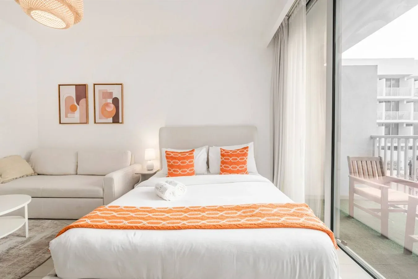 Un dormitorio luminoso con una cama bien tendida y una zona de estar junto a la ventana.