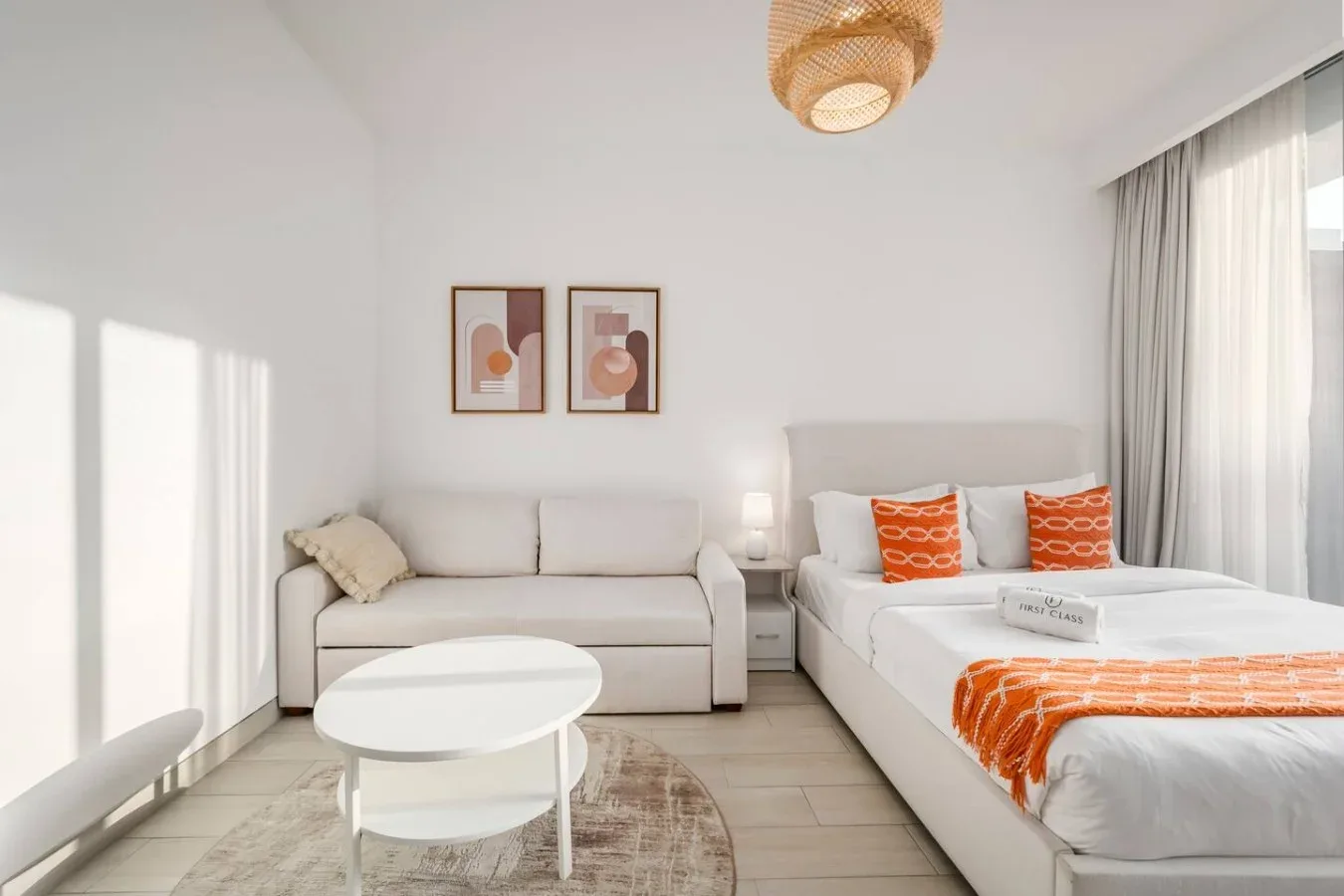 Un dormitorio tipo estudio luminoso con cama, asientos y detalles naranjas.