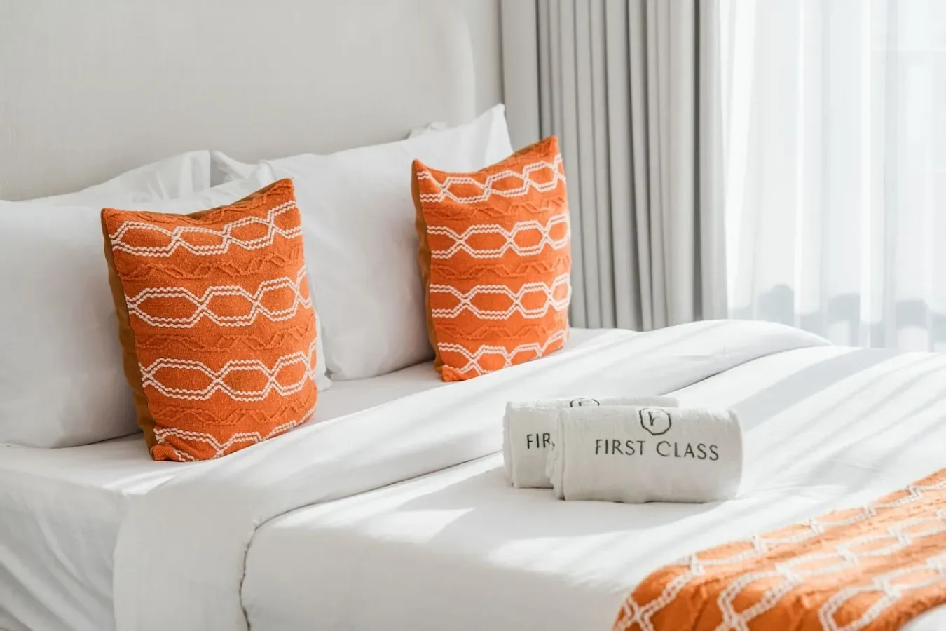 Una cama de dormitorio bien tendida tiene almohadas estampadas naranjas y un camino a juego.