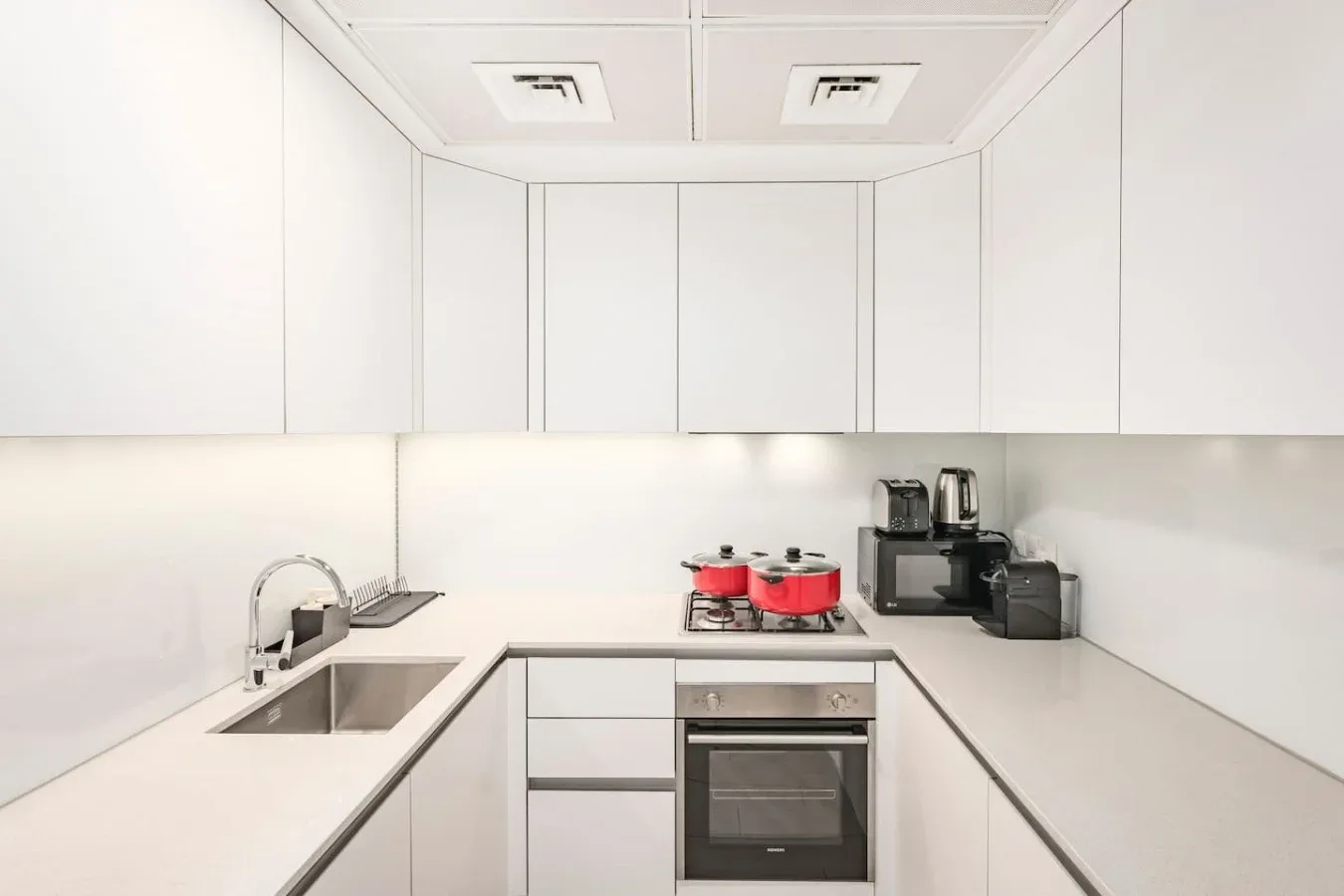 Una cocina luminosa con gabinetes blancos, un fregadero y una placa de cocina.