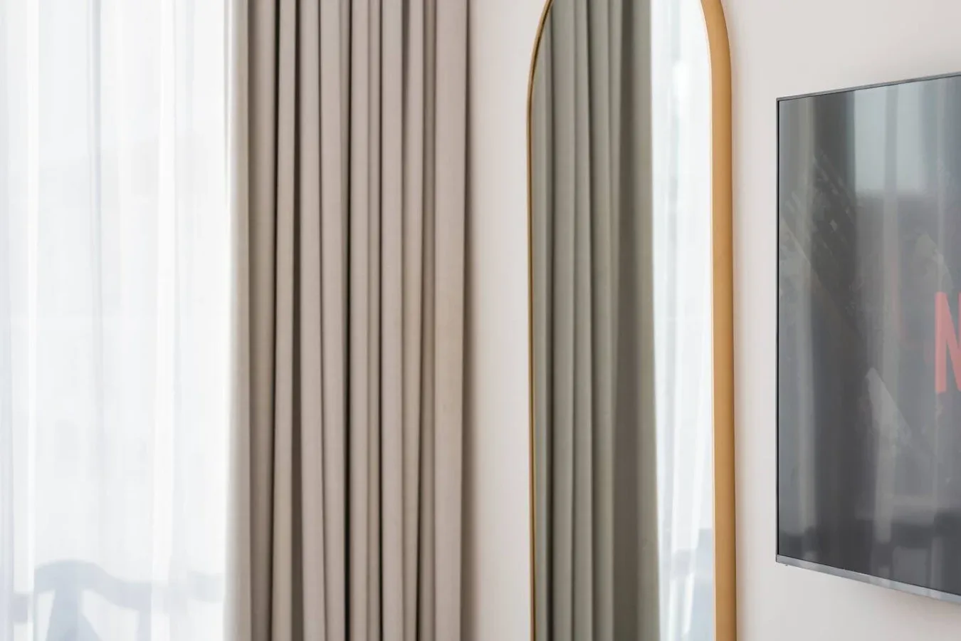 Una ventana con cortinas translúcidas, cortinajes y un televisor montado en la pared.