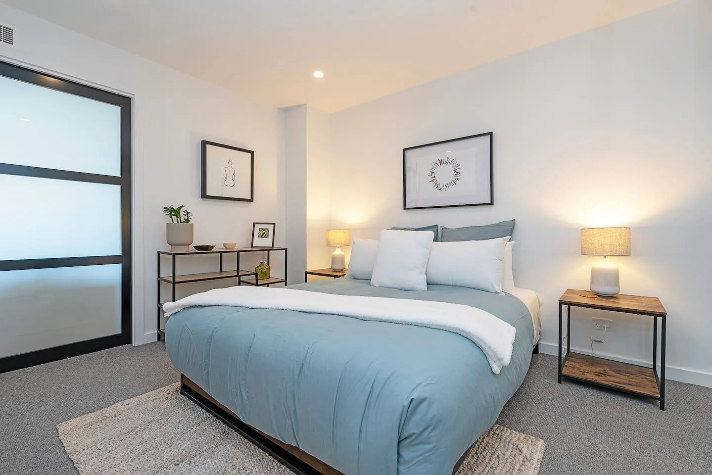 A bedroom with a neatly made bed, bedside tables, and warm lamp lighting.