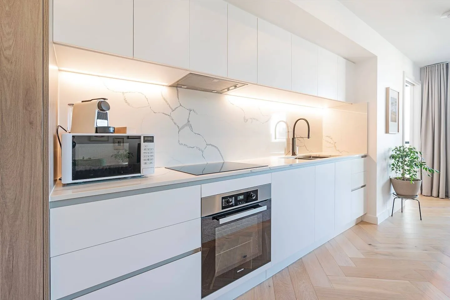 Una cocina moderna con armarios blancos, un horno integrado y una encimera larga.