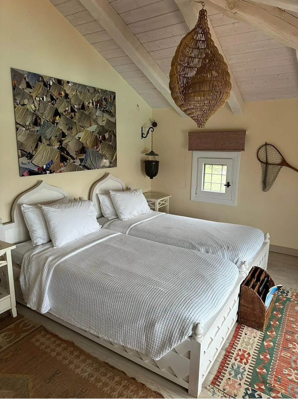 A bedroom with two beds beneath a sloped ceiling and woven pendant light.
