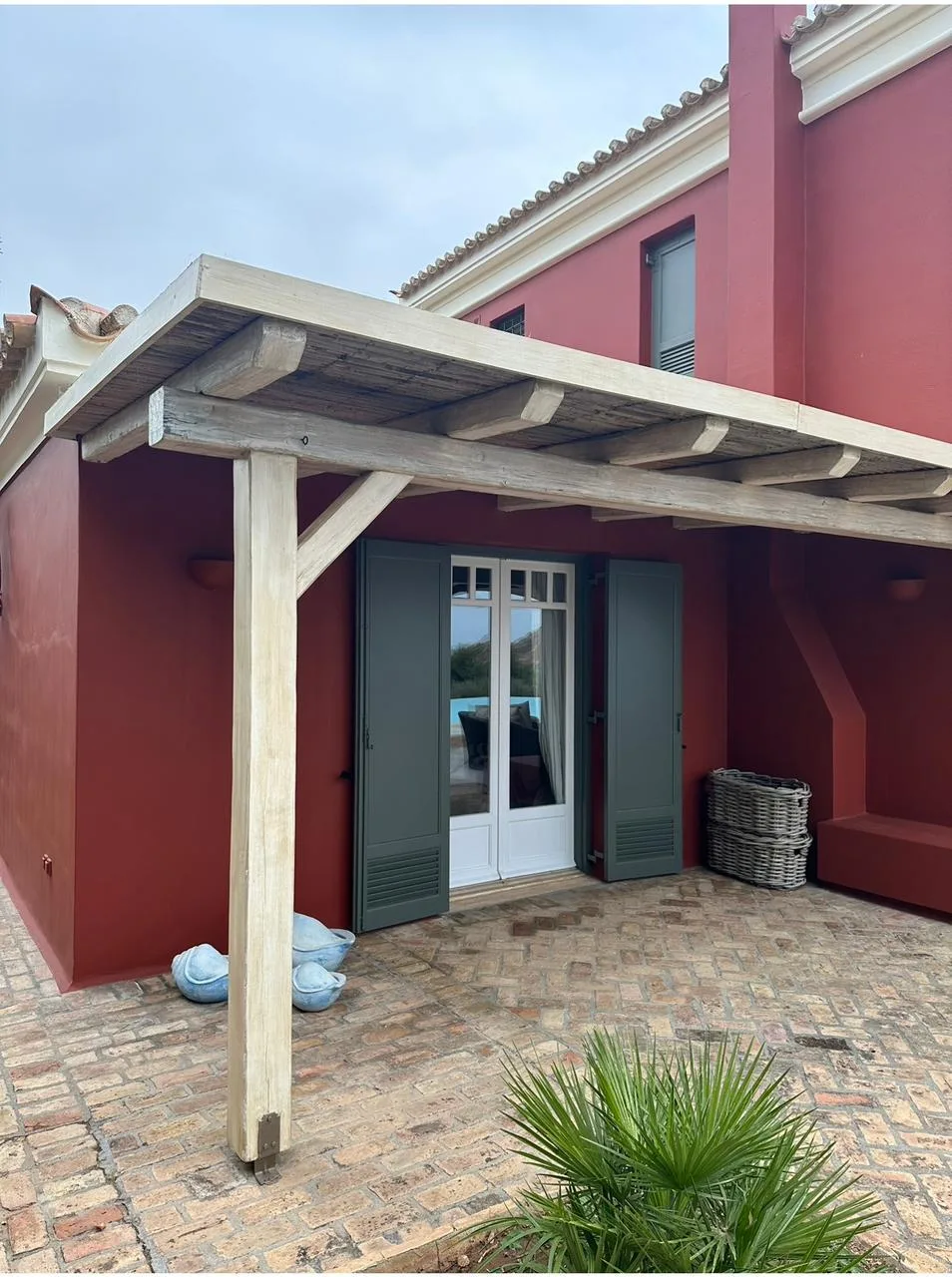 A red exterior patio with a wooden pergola and glass doors.