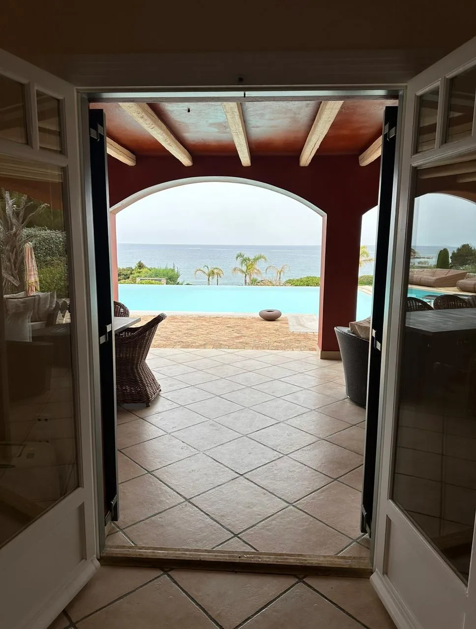 An open doorway frames a tiled terrace, swimming pool, and ocean view.