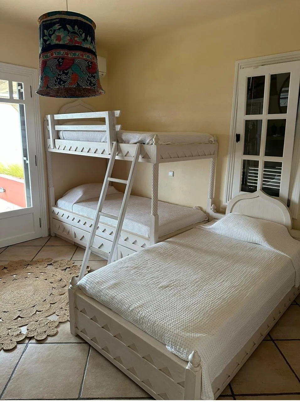A bedroom with a bunk bed and a larger bed beside the window.