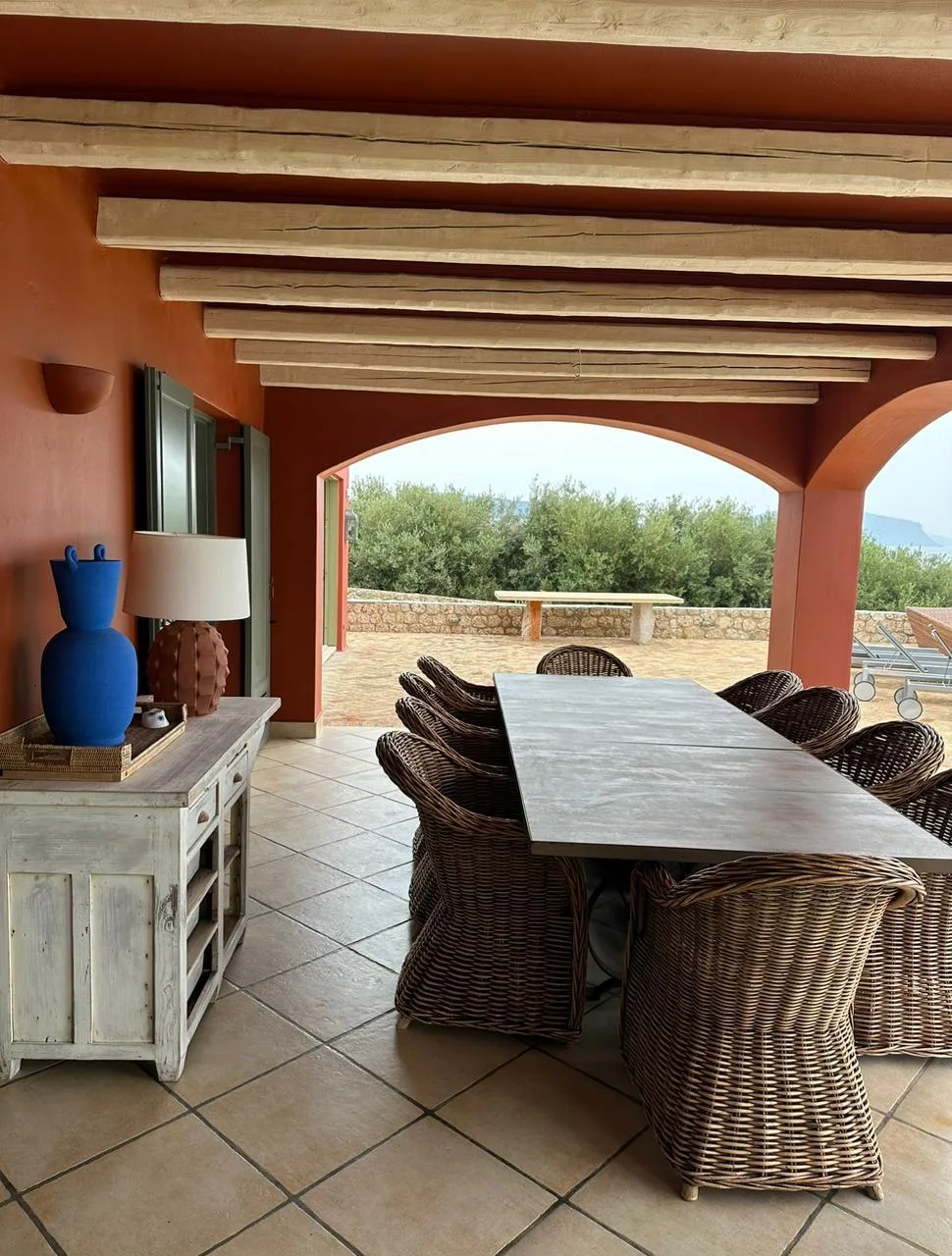 A covered dining area with a long table and woven seating opens onto a terrace.