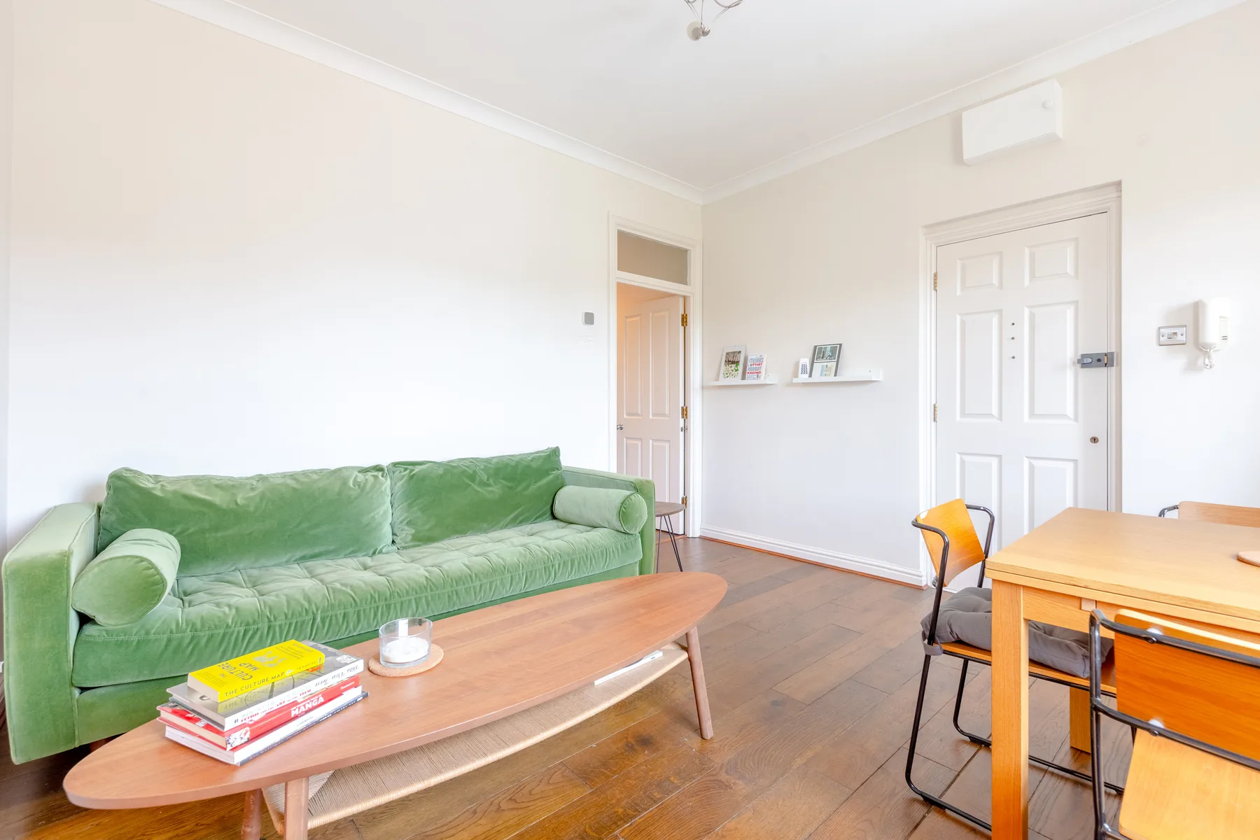 Una habitación luminosa con asientos verdes, una mesa de centro de madera y una mesa de comedor.