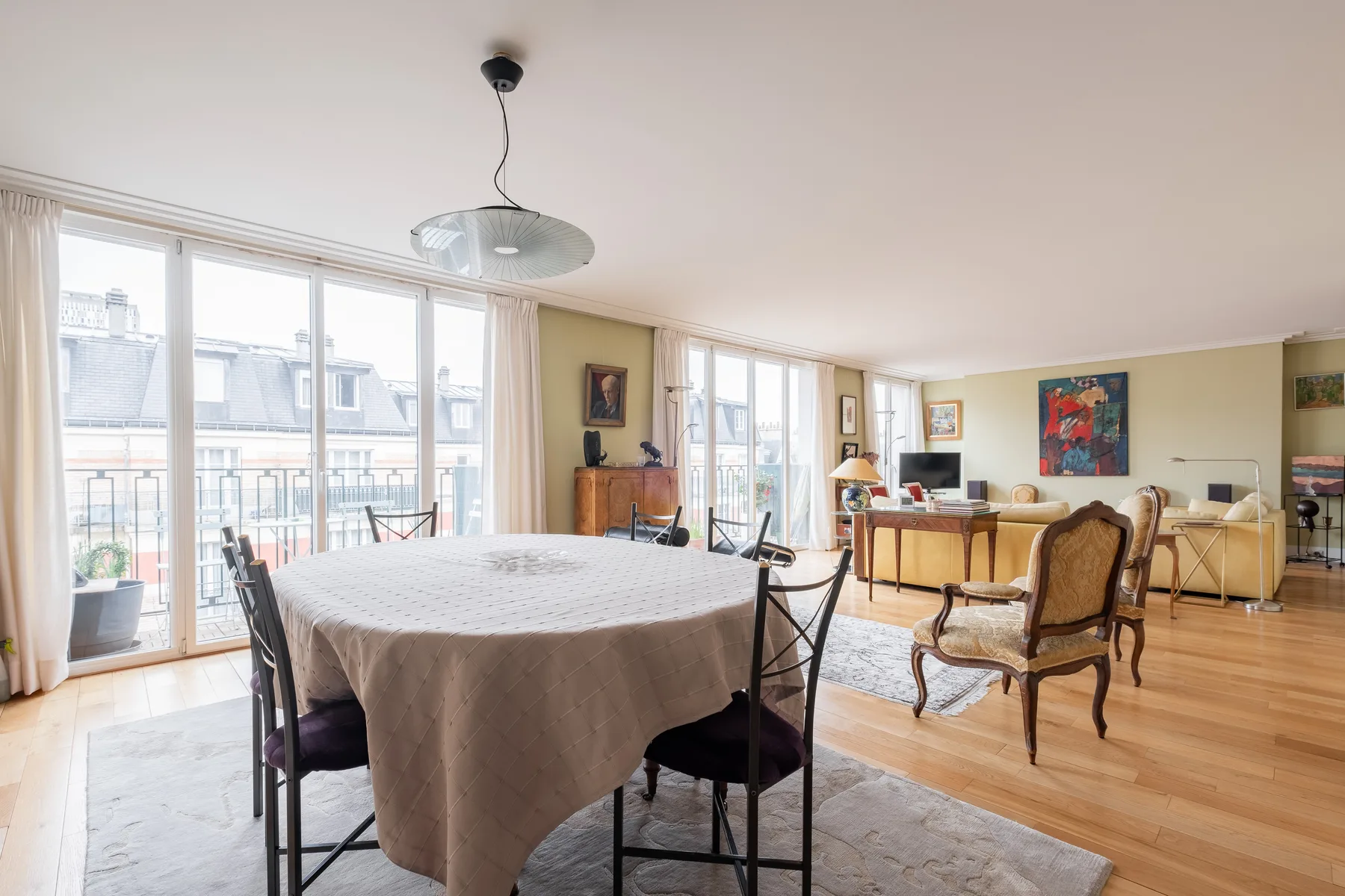 A bright dining and living area with a round table beside large windows.