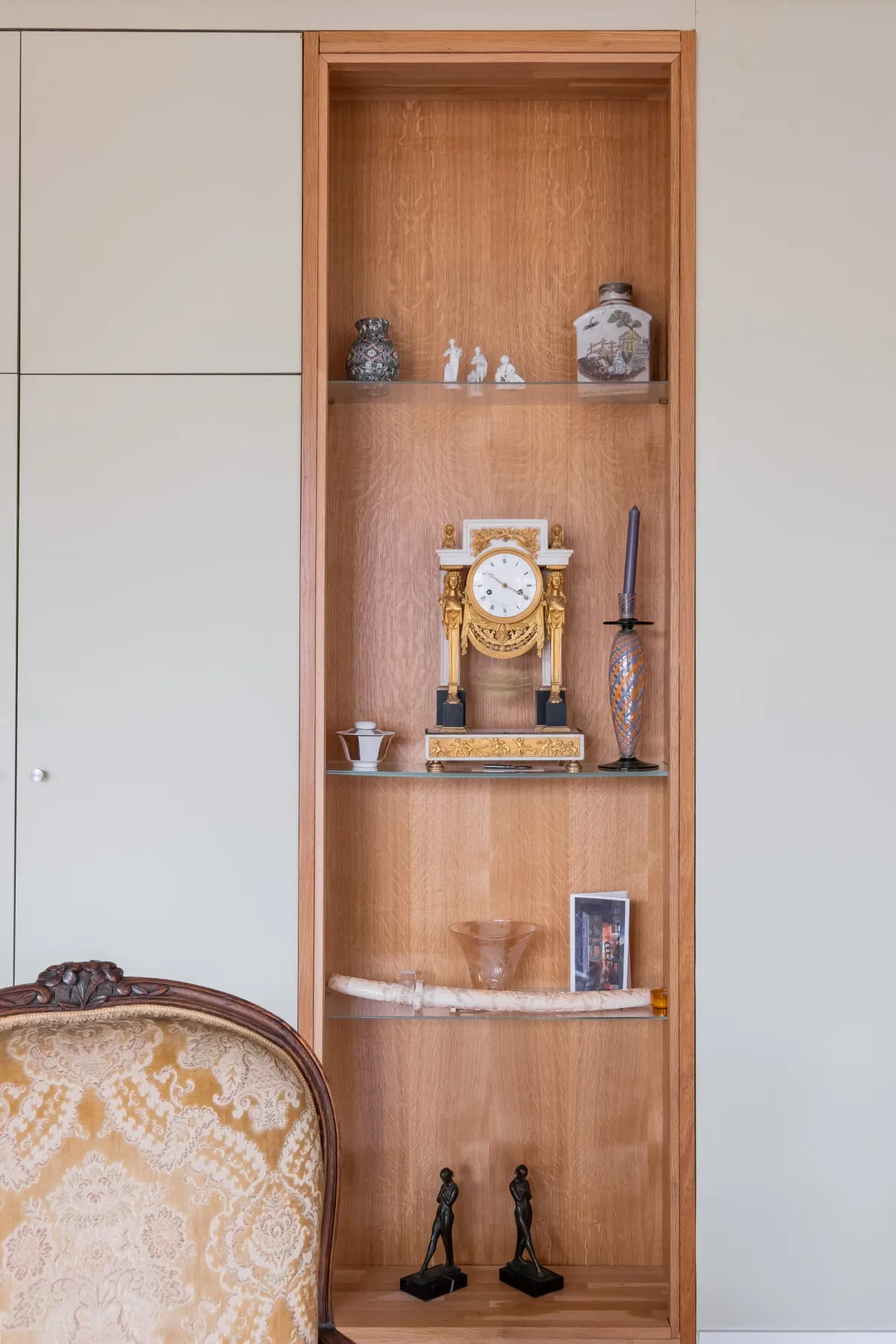 A built-in wooden display shelf holds decorative objects beside a patterned chair.