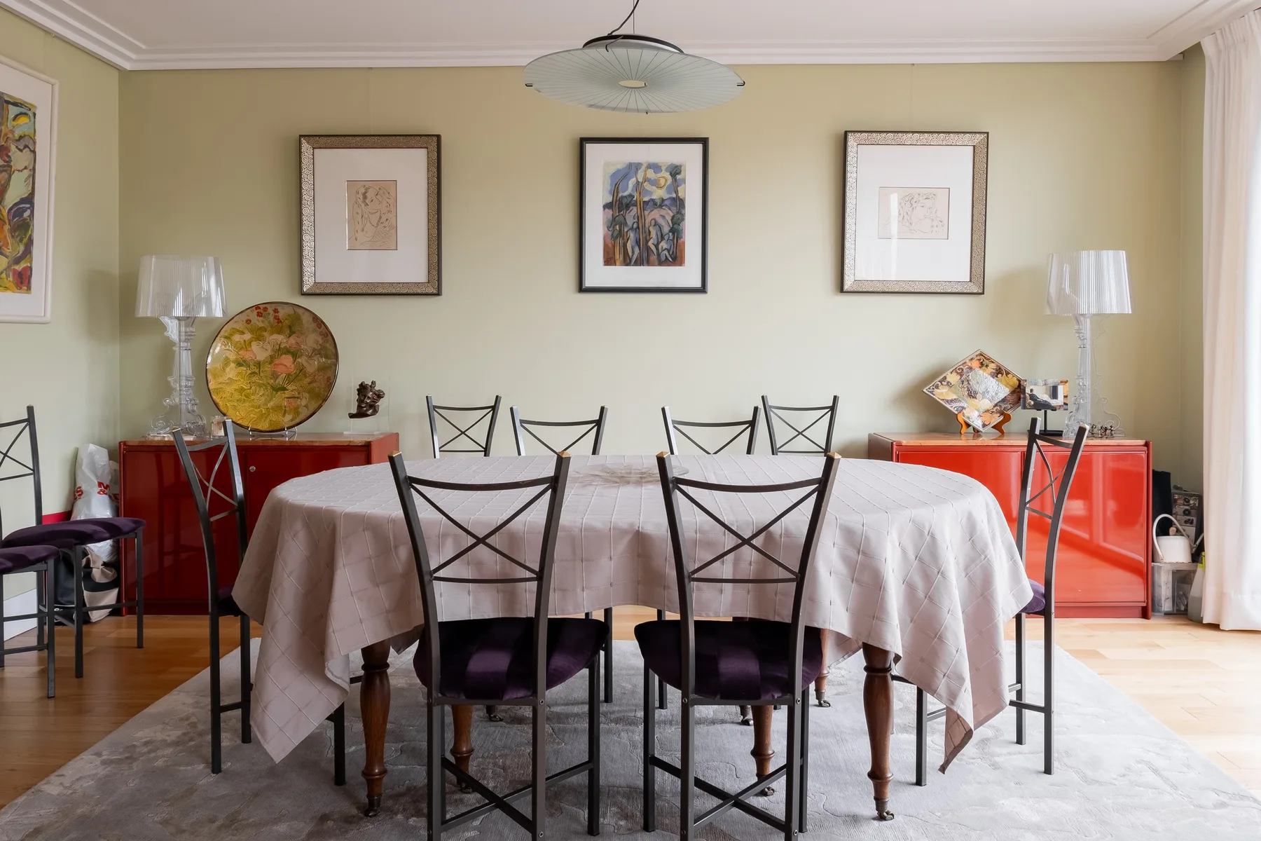 A dining room with a long table, dark seating, and framed artwork on the wall.