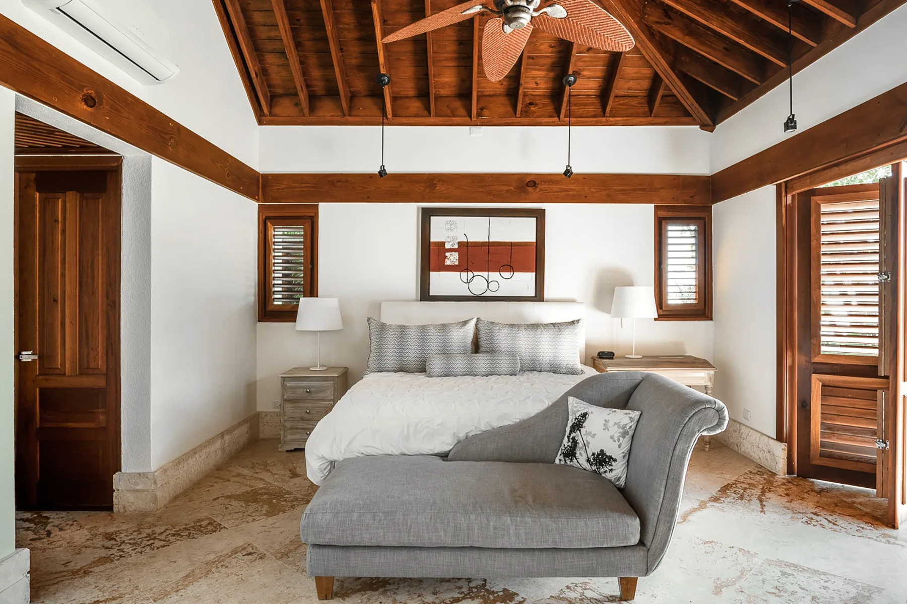 Un dormitorio con una cama grande y un banco gris tapizado a sus pies.