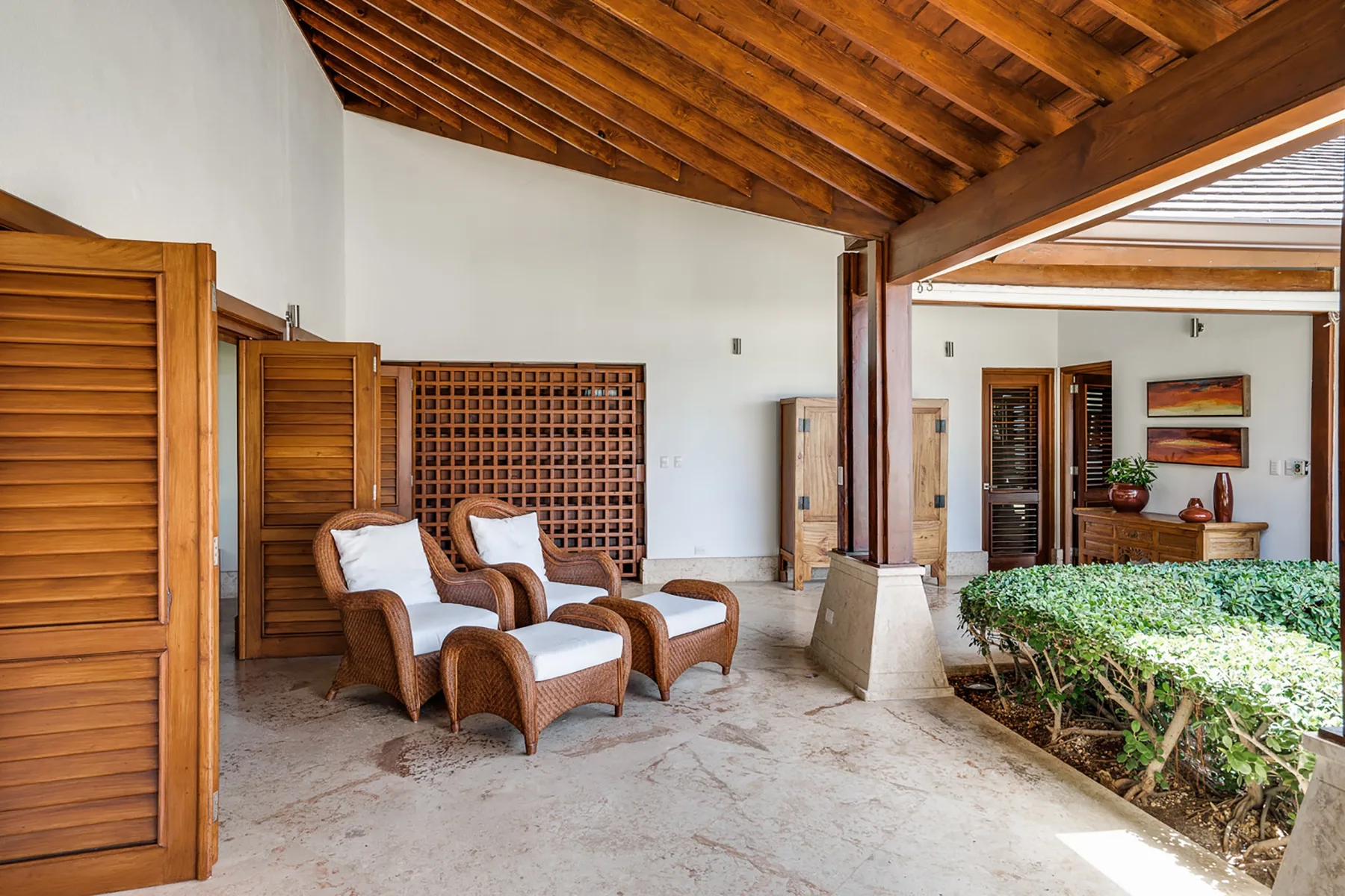 Un patio cubierto con asientos de mimbre junto a un jardín con plantas.