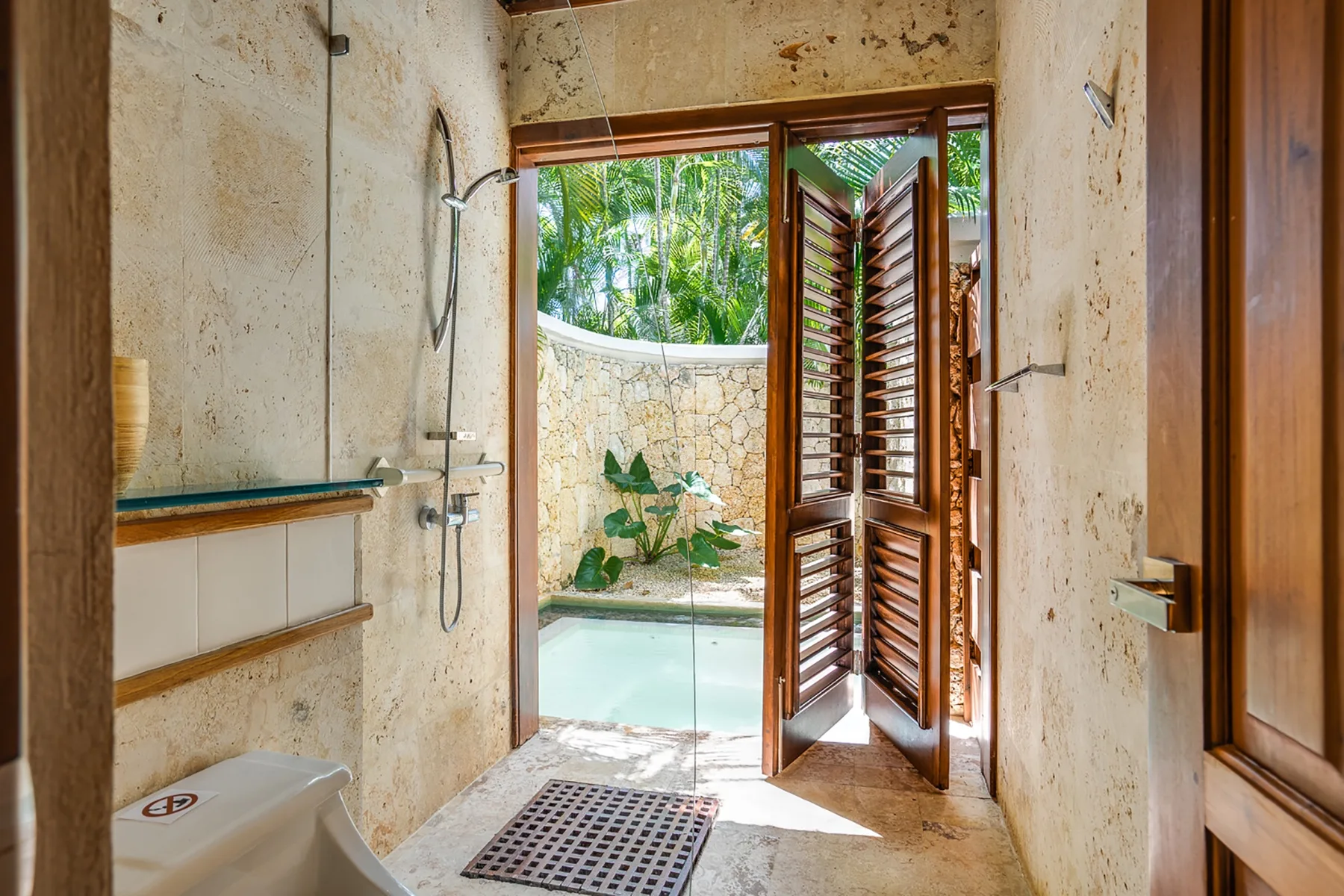 Un baño con una ducha de vidrio y una puerta de madera con celosías abierta.