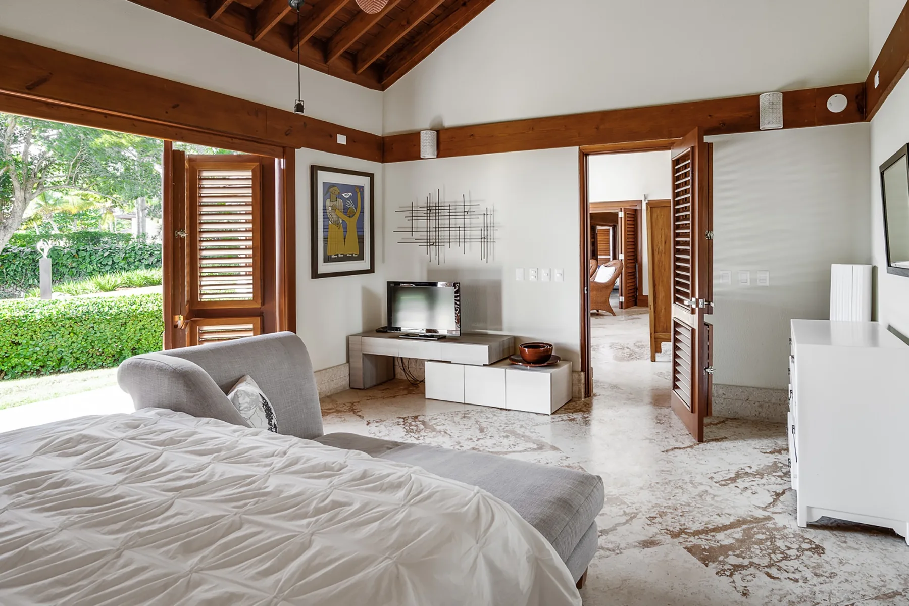 Un dormitorio con una cama, un televisor y puertas abiertas a un jardín.