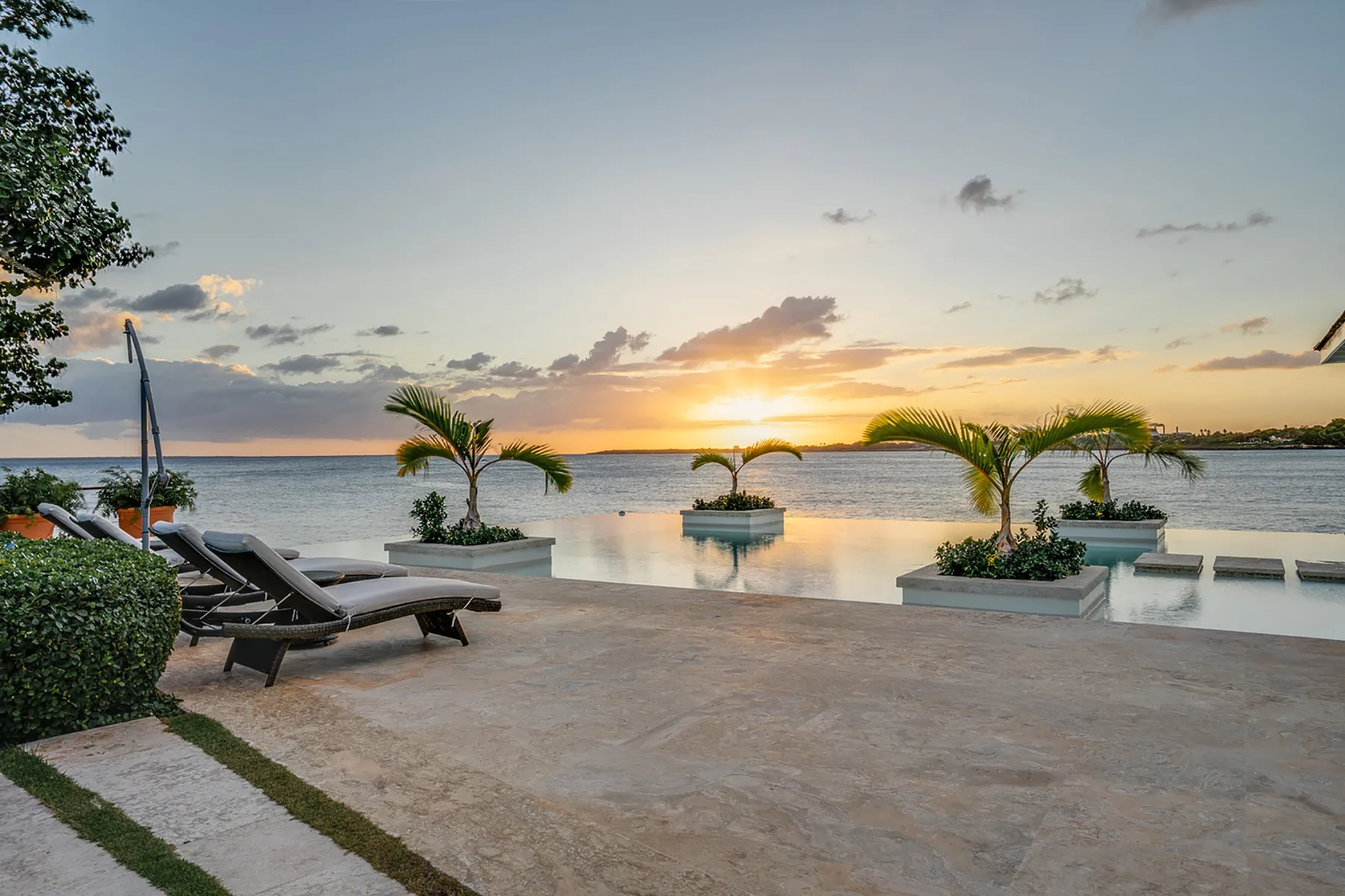Un patio junto al mar contempla el atardecer, con asientos reclinables junto a una piscina reflectante.