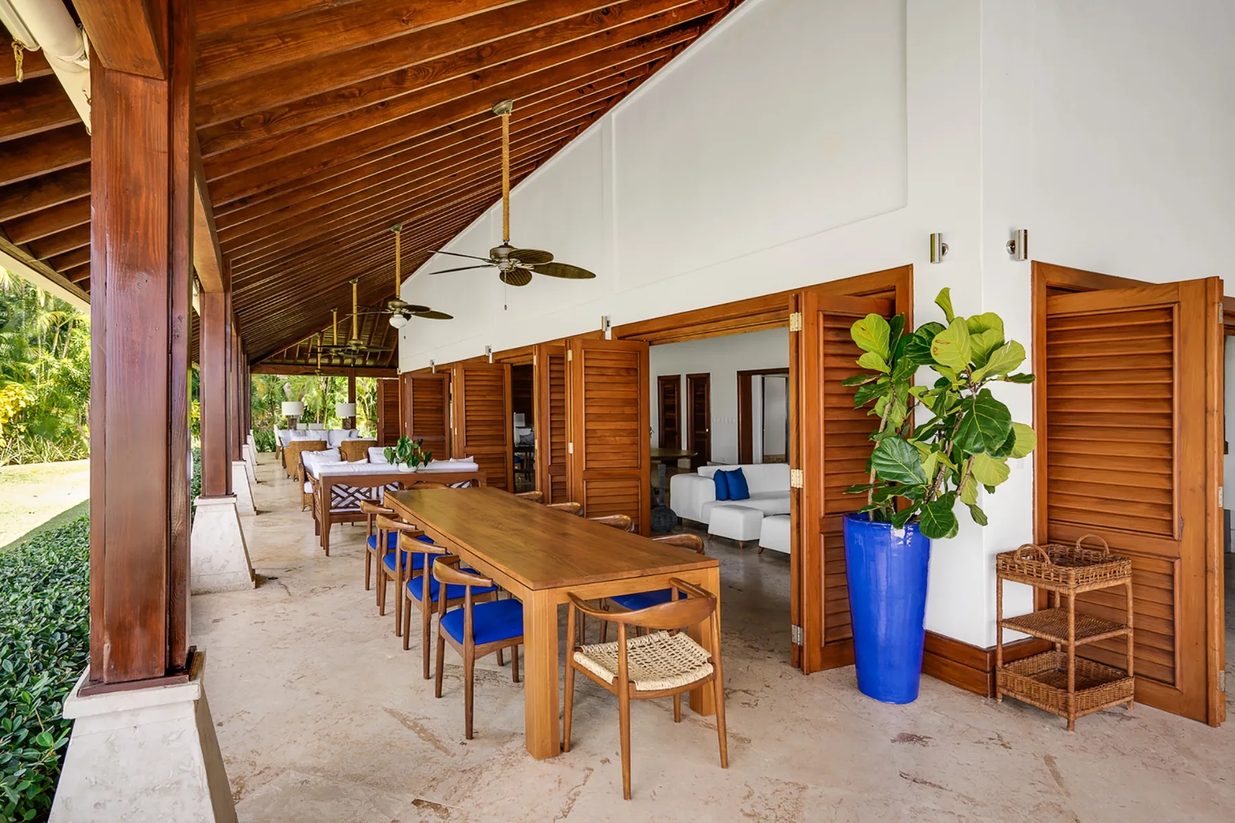 Comedor exterior cubierto con una mesa larga de madera y puertas de celosía abiertas.