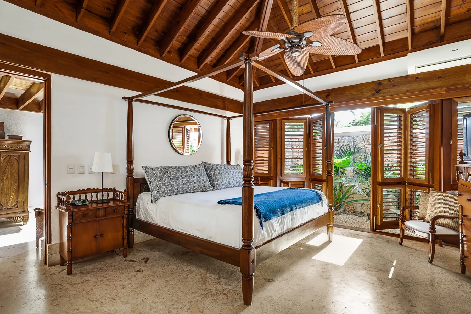 Un dormitorio con una cama con dosel, techo de madera y ventanas con contraventanas.