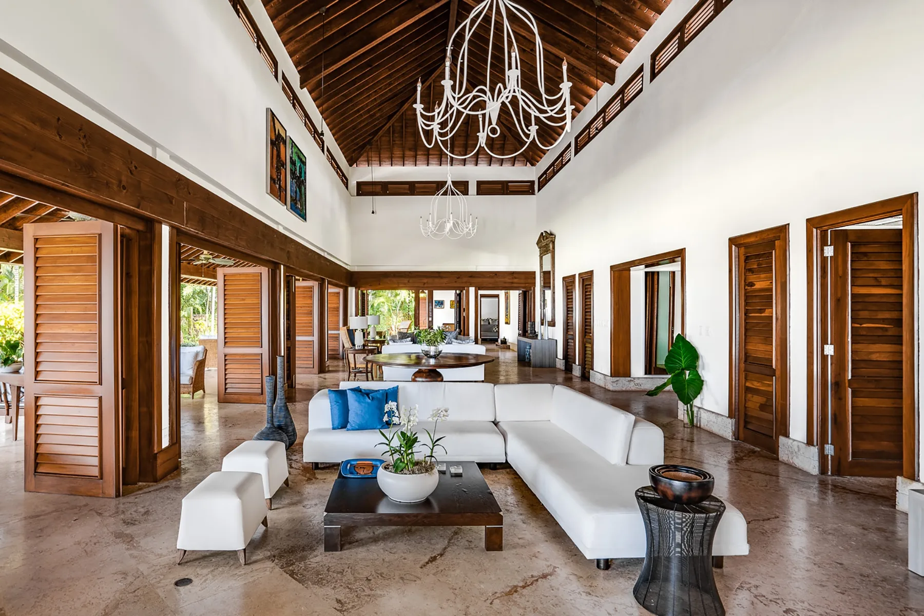 A spacious living room with white seating, wooden doors, and a high timber ceiling.