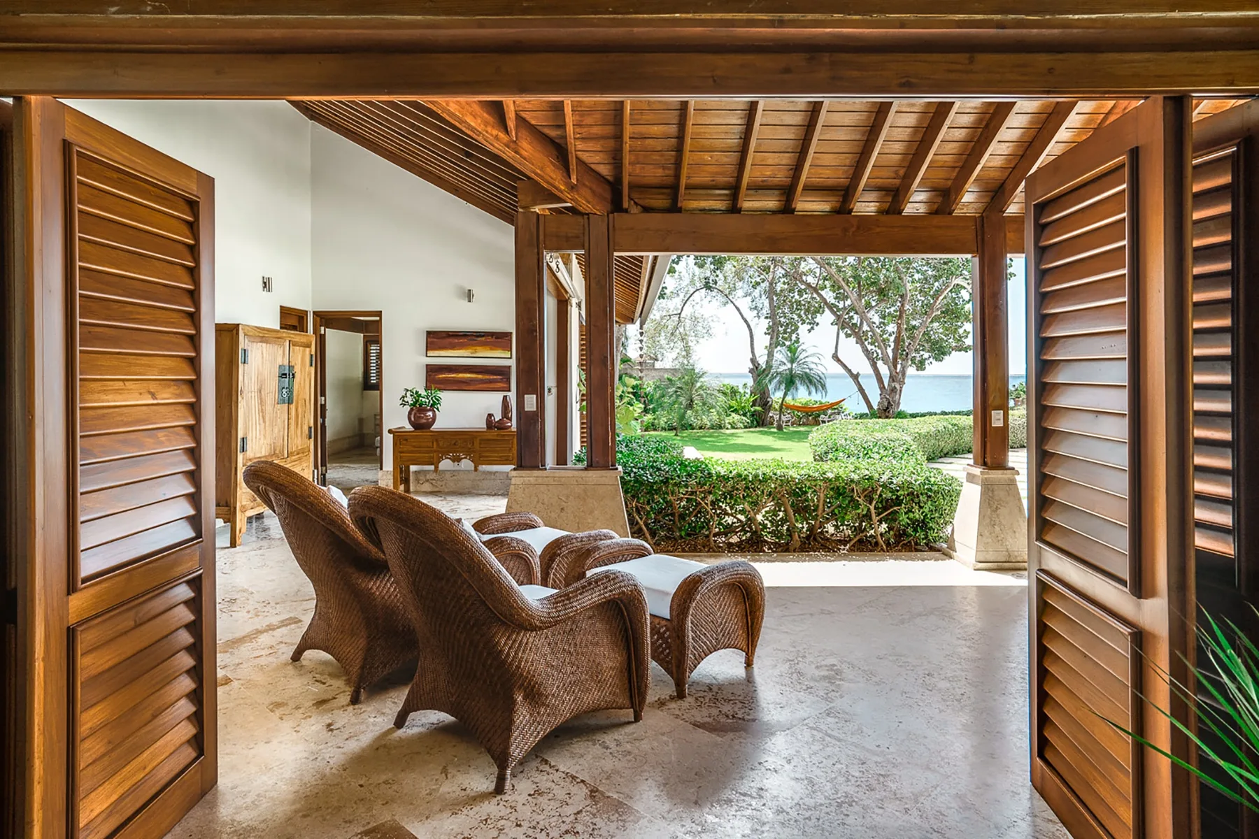 Una zona de estar cubierta y abierta con muebles de madera da a un jardín.