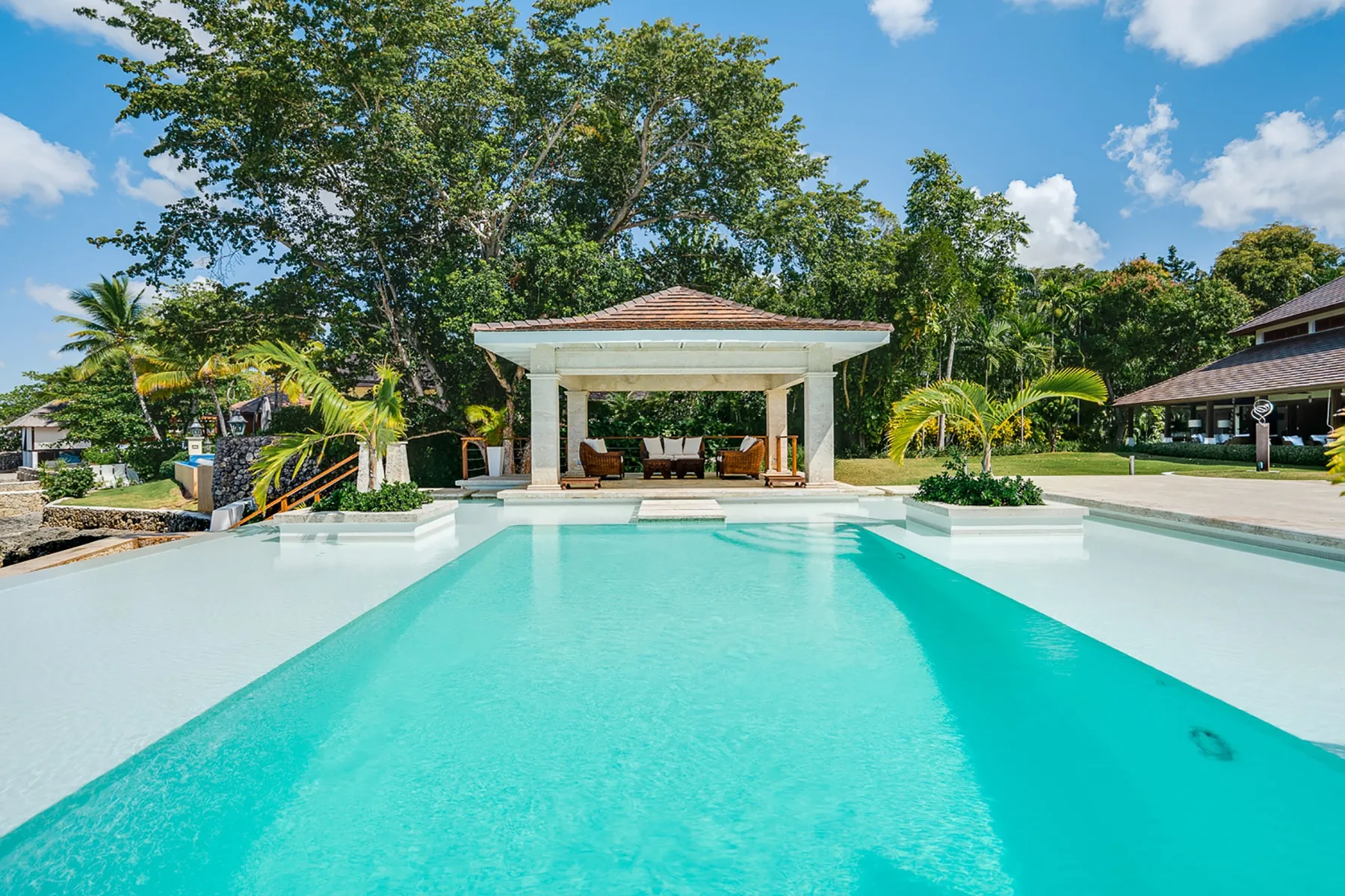 Una piscina se extiende hacia un pabellón sombreado rodeado de vegetación tropical.