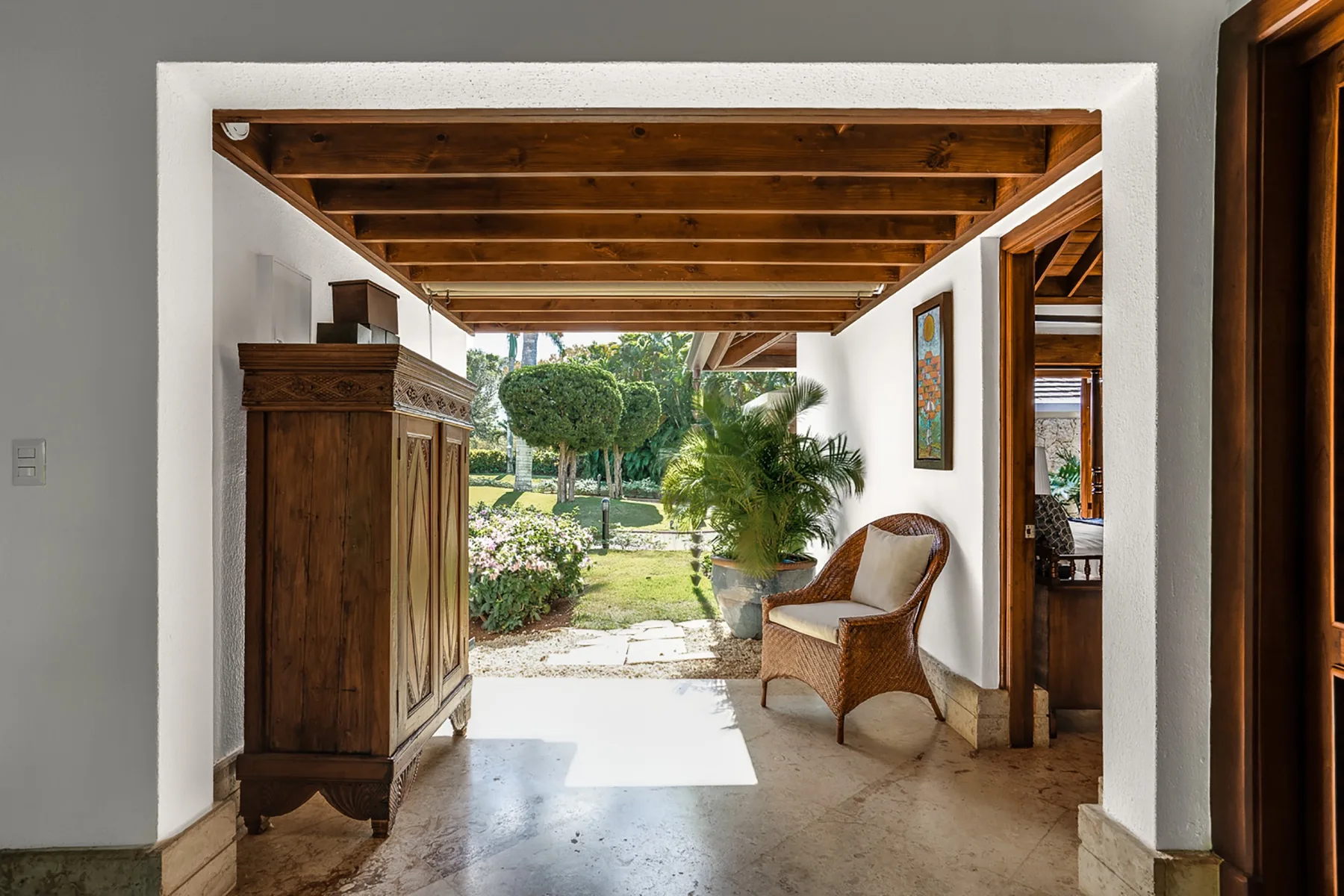 Un patio cubierto da a un jardín, con una silla de mimbre junto a la entrada.