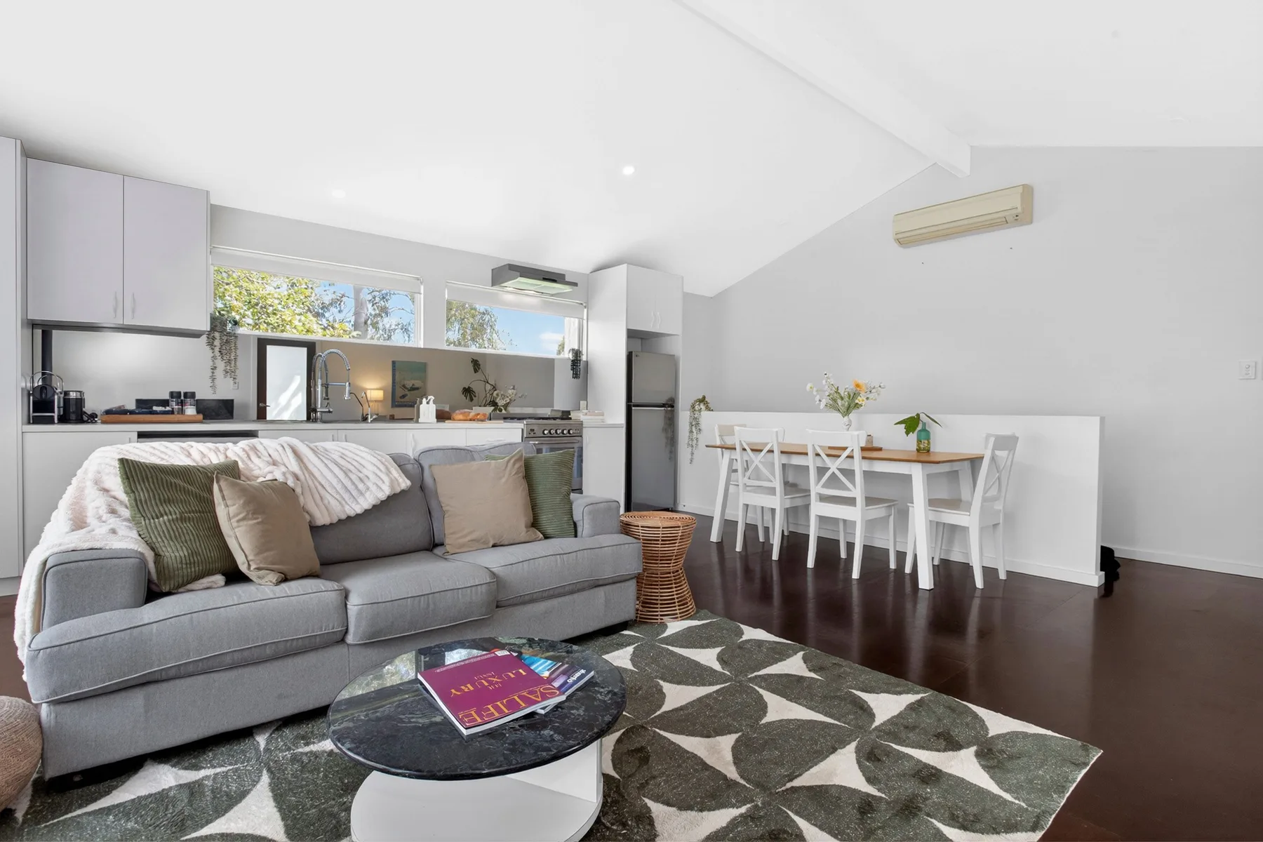A bright open-plan living and dining area with a gray sofa and white table.