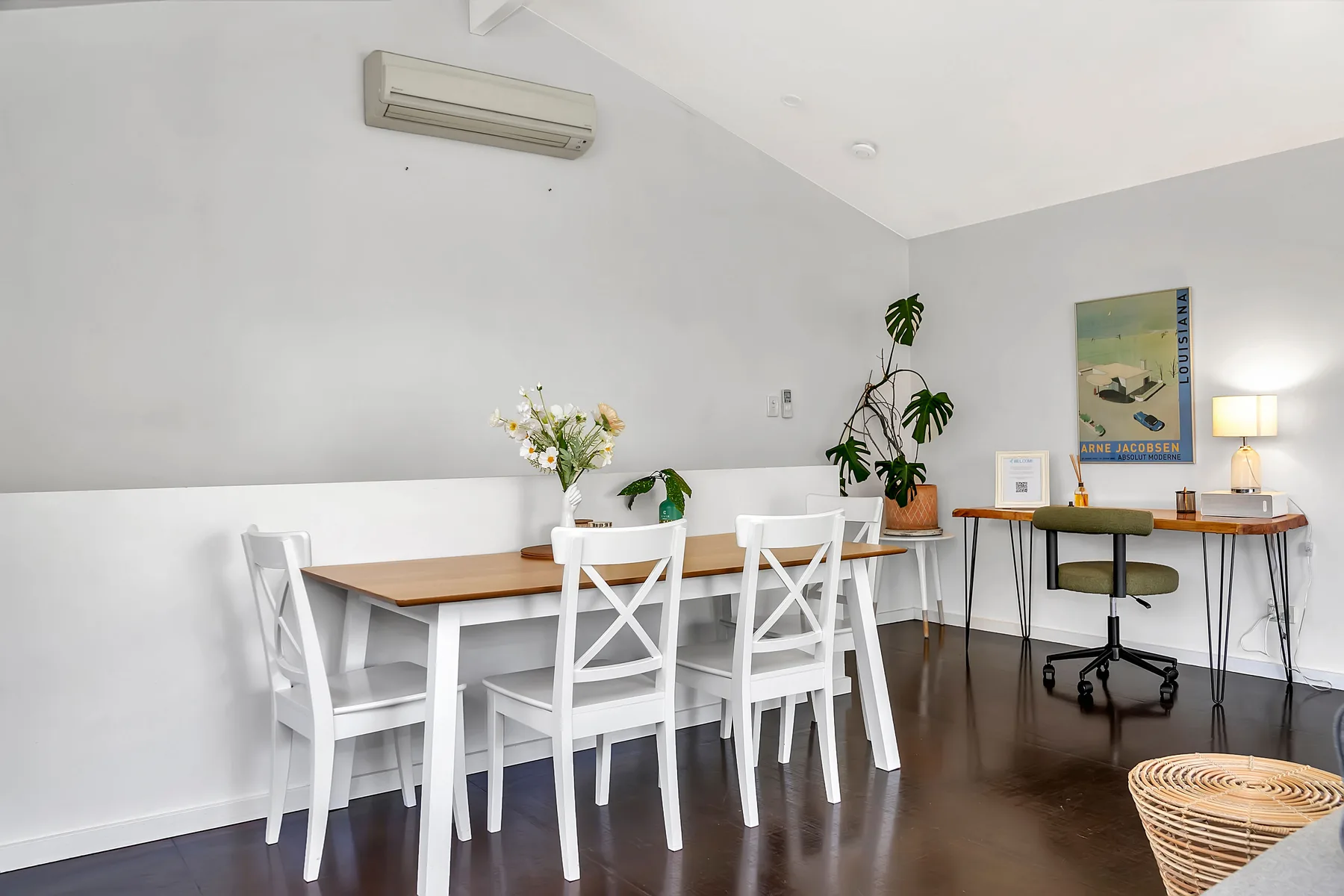 A bright dining and work area has a wooden table, white seating, and a desk.