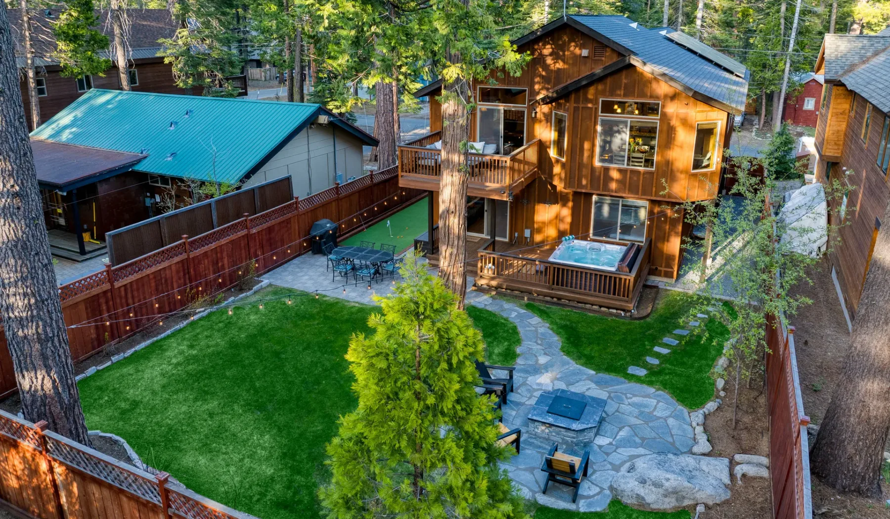 A wooden cabin overlooks a fenced yard with a lawn and stone patio.